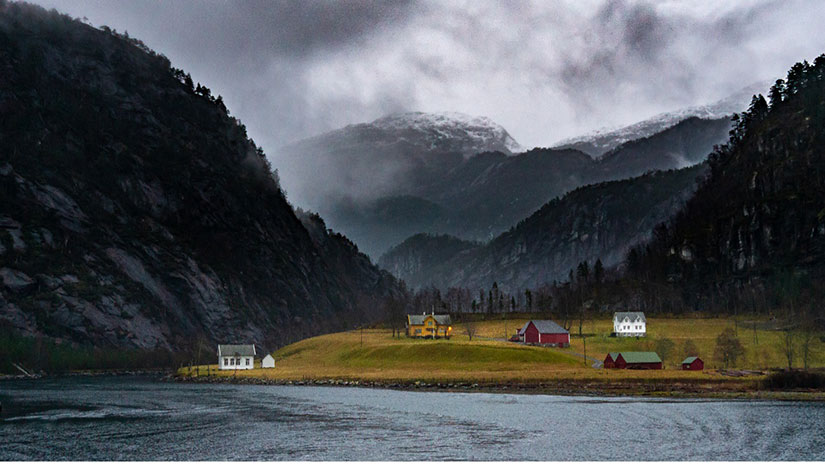 A body of water flowing by a Norwegian village surrounded by mountains