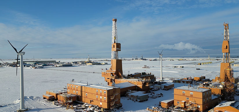 Two small wind turbines at the edge of a campus of buildings on a snowy landscape.