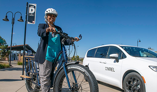 Photo of a woman standing in a parked position on a bicycle next to a car.