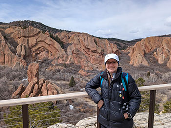 Genevieve Starke wearing hiking gear and standing against a railing in front of a rocky landscape.