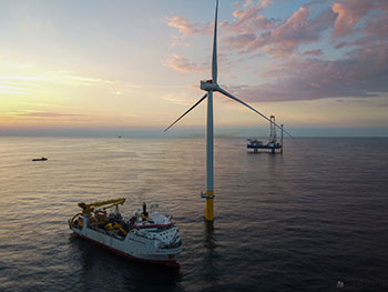 Photo of an offshore wind turbine with a servicing ship next to it in the ocean