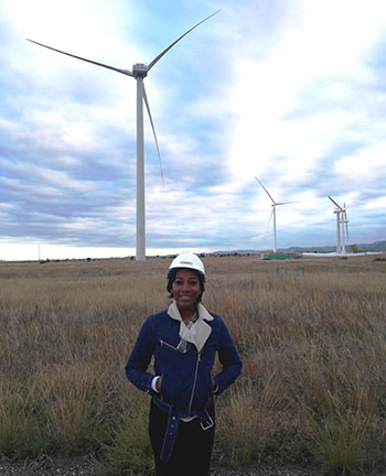Angel McCoy in a hardhat standing in front of a group of wind turbines