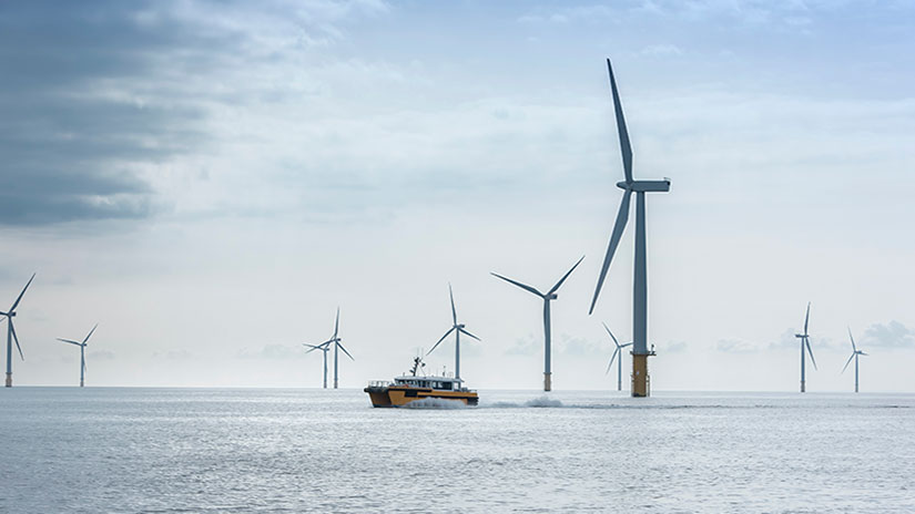 A boat sits on the water amidst nine offshore wind turbines.