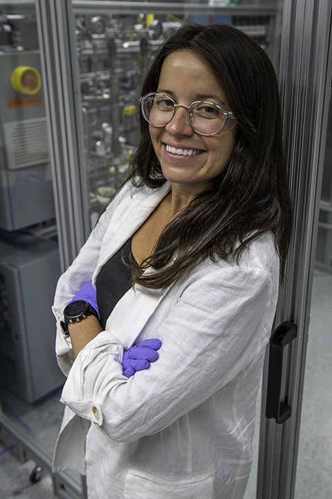 A woman wearing gloves and glasses poses in a lab. 