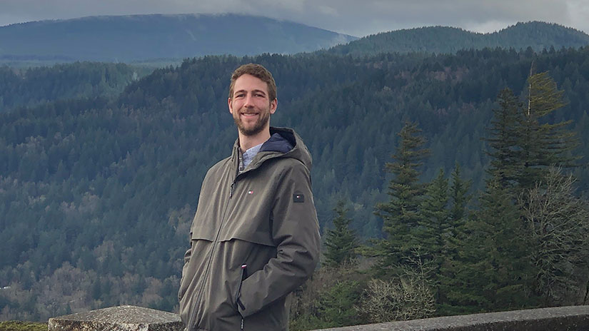 Alec Schnabel standing in front of a vista of evergreen-covered hills