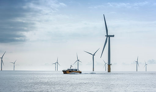 A boat sits on the water amidst nine offshore wind turbines