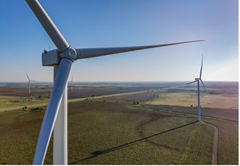 An aerial photo of a wind turbine standing over farmland, with more wind turbines in the background.