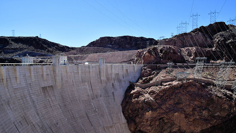 A large dam with electrical transmission lines crossing over a cliff nearby
