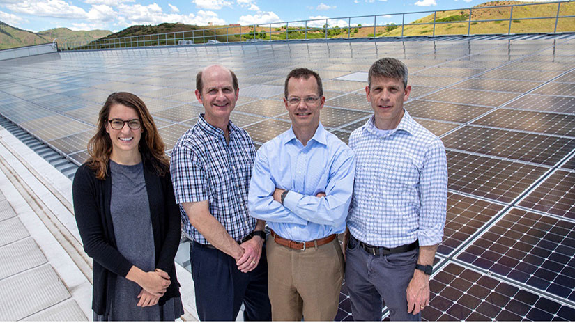 Four people posing in front of solar panels