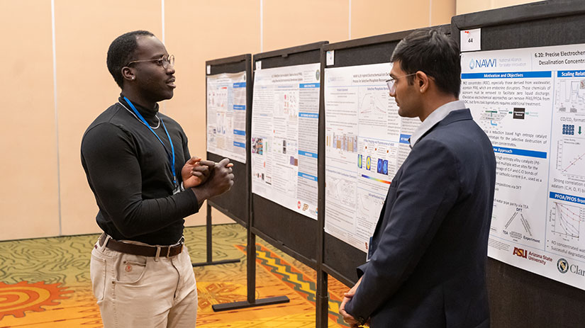 Two people discuss research poster inside hotel ballroom