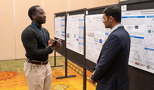 Two people discuss a research poster inside a hotel ballroom