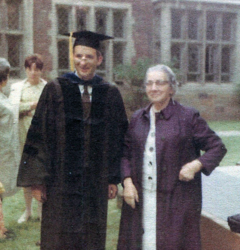 An old photo of a young man in a college graduation gown standing next to his mother
