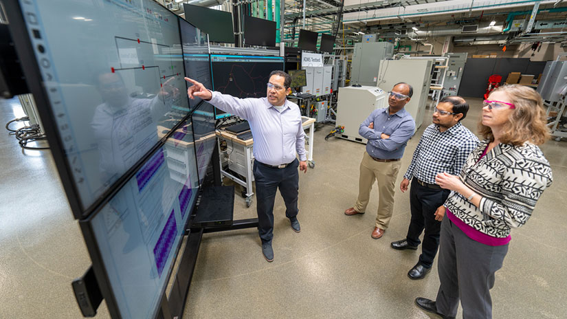 Four researchers in a laboratory review data on a large screen