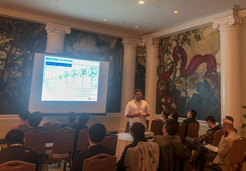 A person presenting a slide with wind turbine diagrams on it to a room of people.