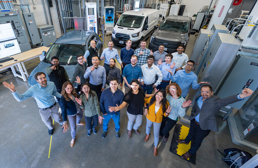 A large group of people in a lab with three vehicles looking up.