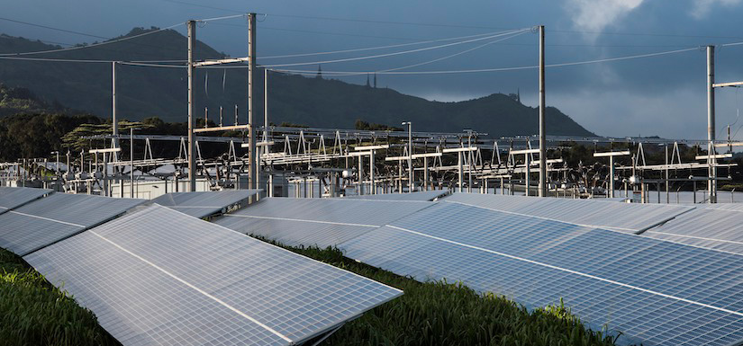 A power substation stands behind a field of tilted solar panels.