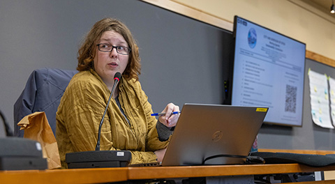 A woman sitting behind a laptop speaking into a microphone.