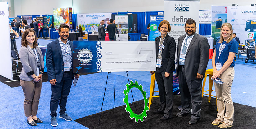 Five people smile standing next to a giant blank check at a conference.