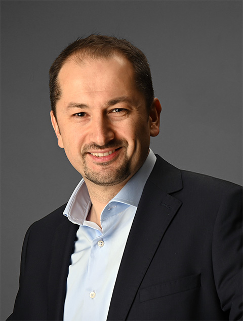 Portrait of a smiling man in a light-blue button-down shirt and black blazer.