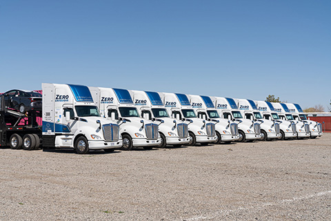 A fleet of 10 hydrogen fuel cell trucks parked in a line against a bright blue sky.