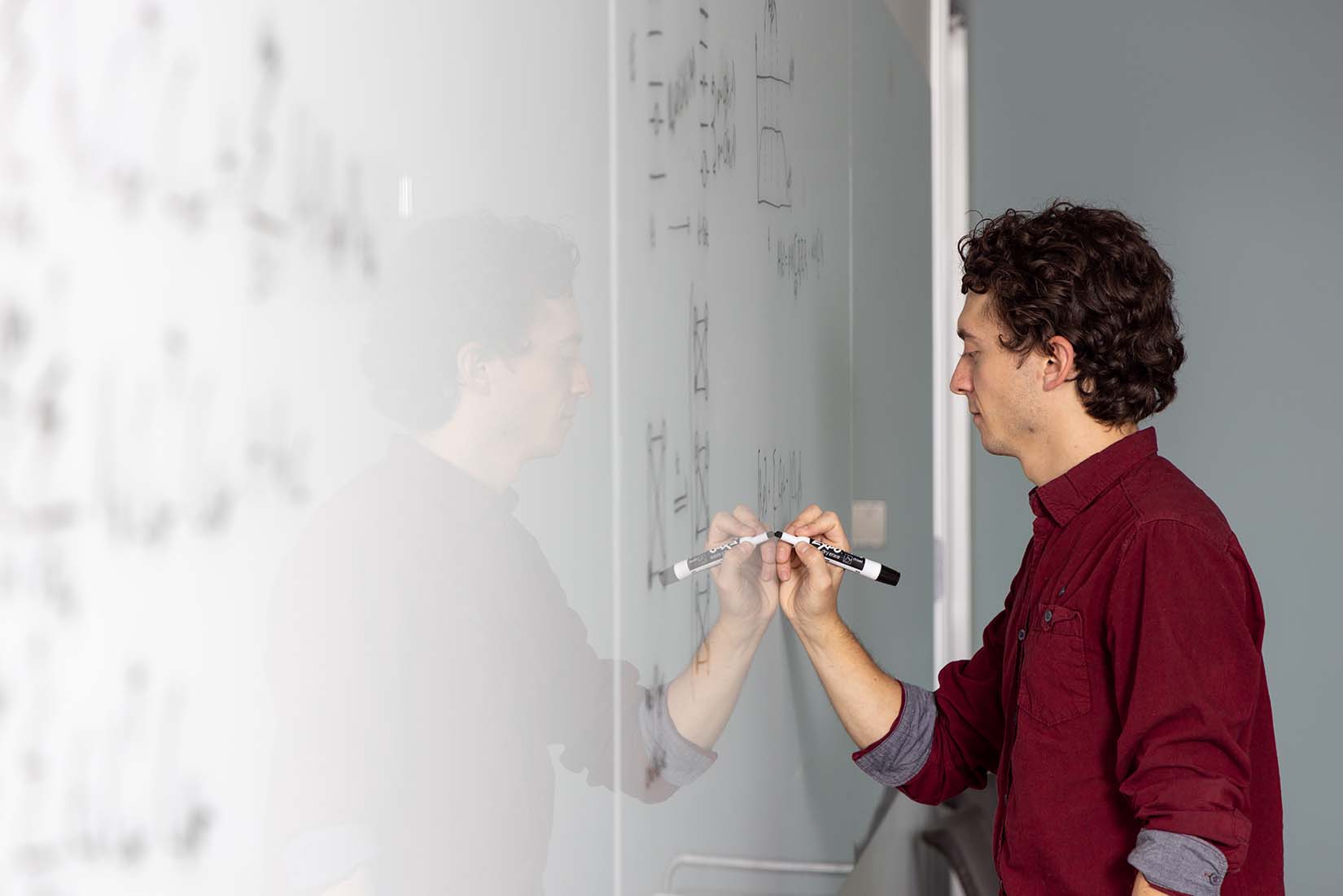 Scientist writing on a whiteboard as part of his research process into quantum computing benchmark problems