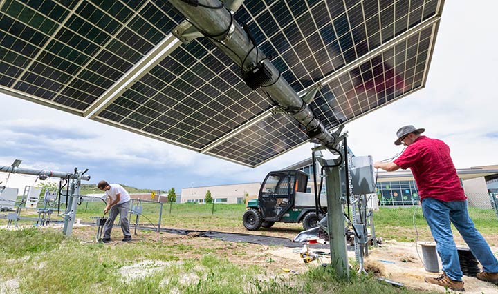 Photo of the PV cells on the underside of bifacial solar panels, with two men installing the system in the background.