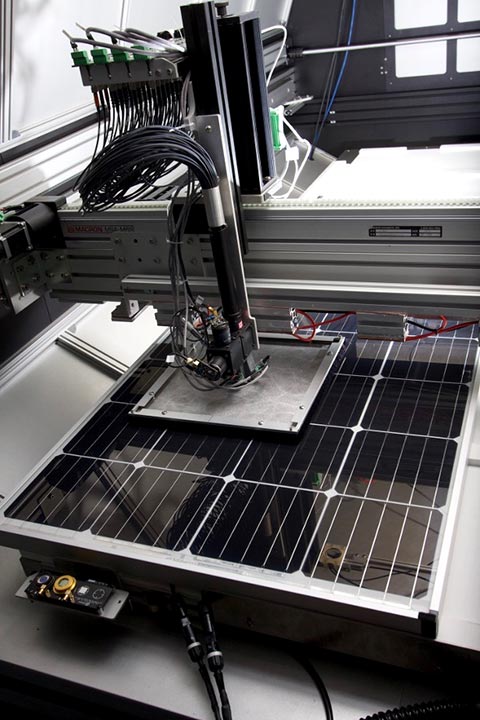A solar module sits underneath a square shade that covers several cells around the measured cell. A bundle of black fibers runs from LEDs to the center of this shade to measure the desired cell.