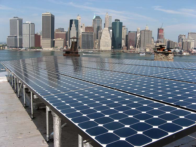 Solar photovoltaic system on a city building rooftop with skyscrapers in the background.
