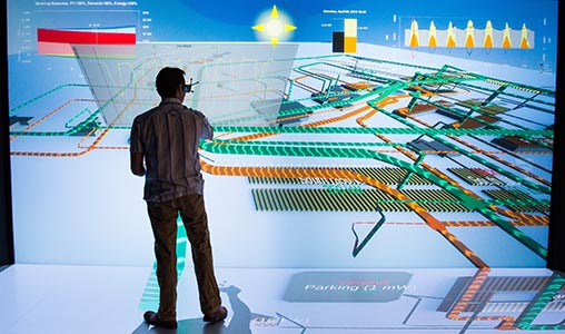 NREL scientist working in front of a wall-sized energy system design schematic in a 3-D visualization laboratory.