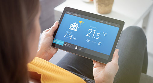 A woman looking at a tablet with smart home monitoring on the screen.