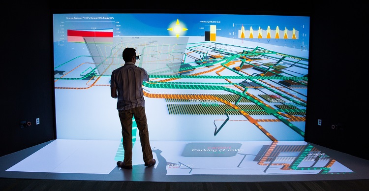 NREL scientist working in front of a wall-sized energy system design schematic in a 3-D visualization laboratory.