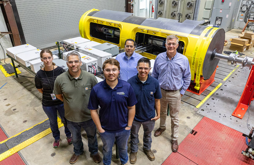 Six researchers stand in front of a yellow, cylindrical device and boxes of electronics.