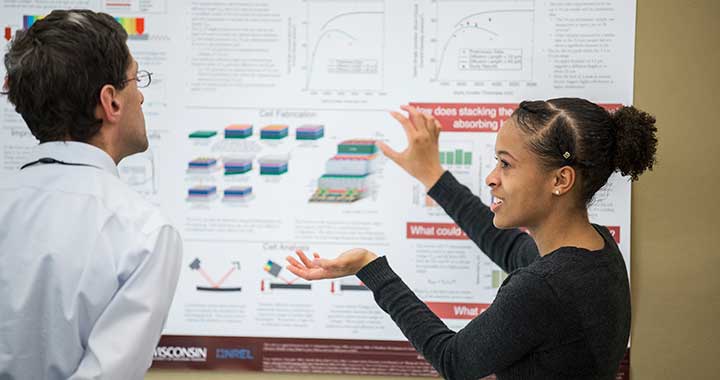 An intern presents research poster to another person.