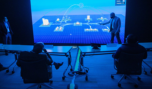 People sit in front of large computer display while another person presents data on the screen