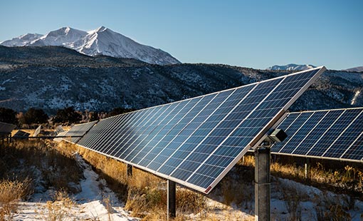 Photo of solar panels with mountains in the foreground. 