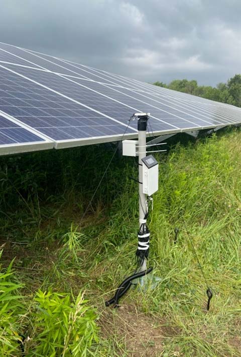 A suite of sensors sits on the ground at the base of a solar panel array.