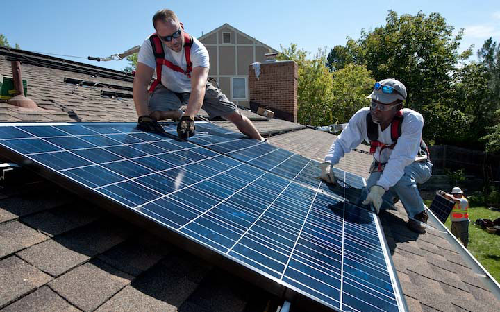 Two men installing solar panels on the roof of a house.