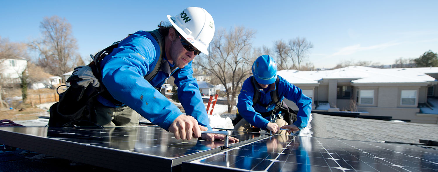 Two workers in hard hats assemble pv panels on a roof.