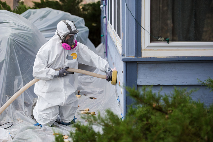 A weatherization professional in a safety suit injects insulation into the exterior walls of a home.