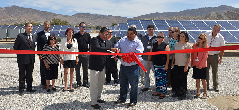 Tribal Council members and partners cut a ribbon in front of a solar panel system.