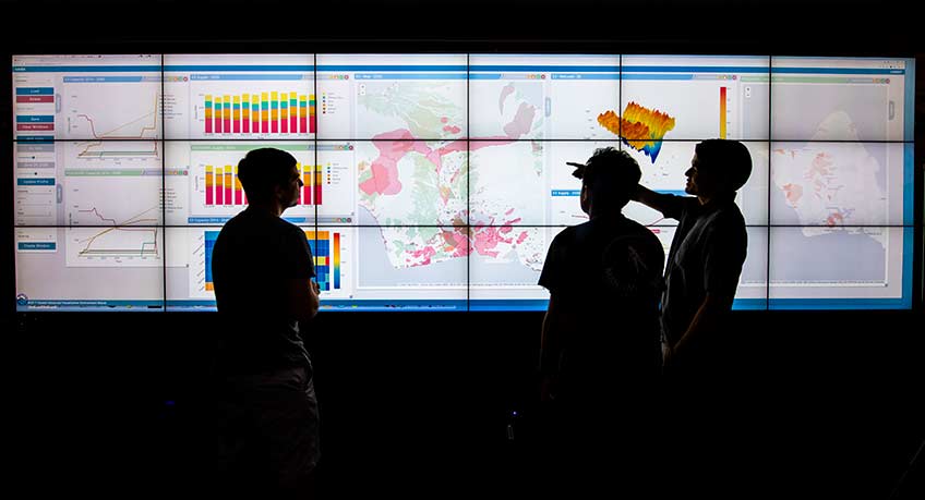 Three people looking at a wall-sized, data visualization.