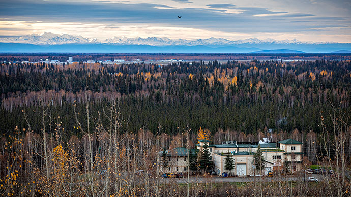 A photo in Fairbanks, Alaska with snowy mountain ranges in the distance, and trees and a research facility building in the foreground.