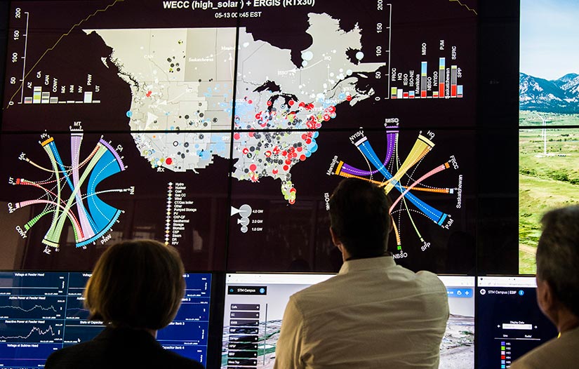 Researchers looking at large monitors with charts of data surrounding a map of North America.