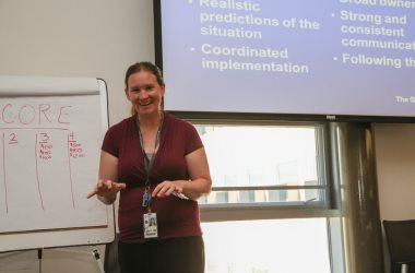 Photo of a female laughing while standing in front of a projector and white board.