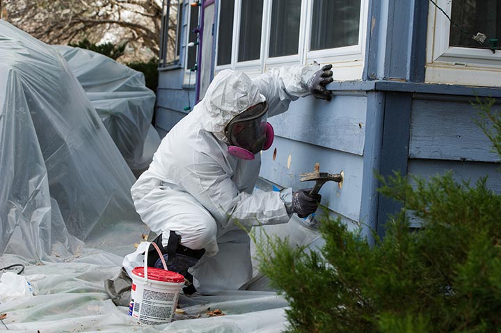 A photo of a home weatherization professional working on the base of a home.