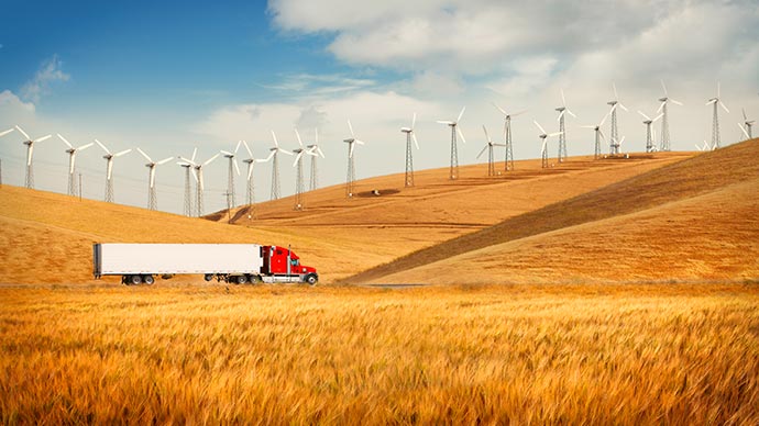 Truck driving through the countryside with many wind turbines in the background.