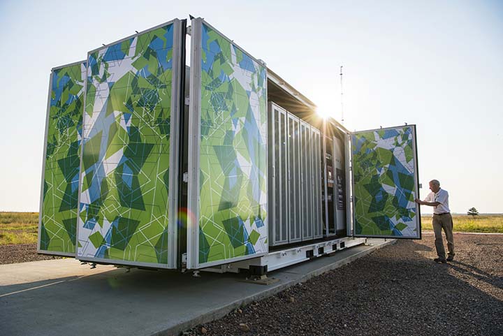 Flex manufactured battery enclosure decorated in green and blue geometric shapes at the Battery Energy Storage System site at NREL's National Wind Technology Center.
