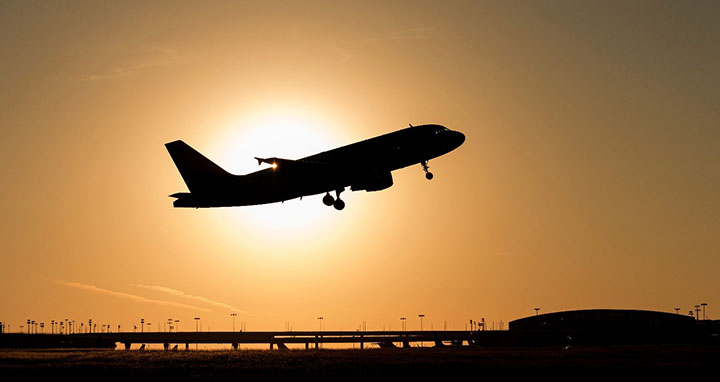 A silhouette of a plane taking off in front of the rising sun.