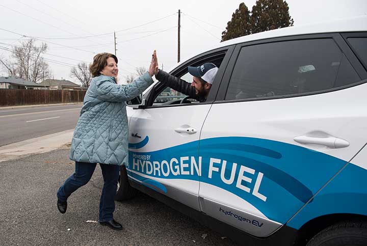 Two volunteers high five through the window of a hydrogen fuel vehicle.