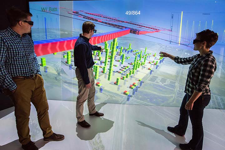 Three researchers wearing special goggles look at a 3D energy model displayed on a large screen